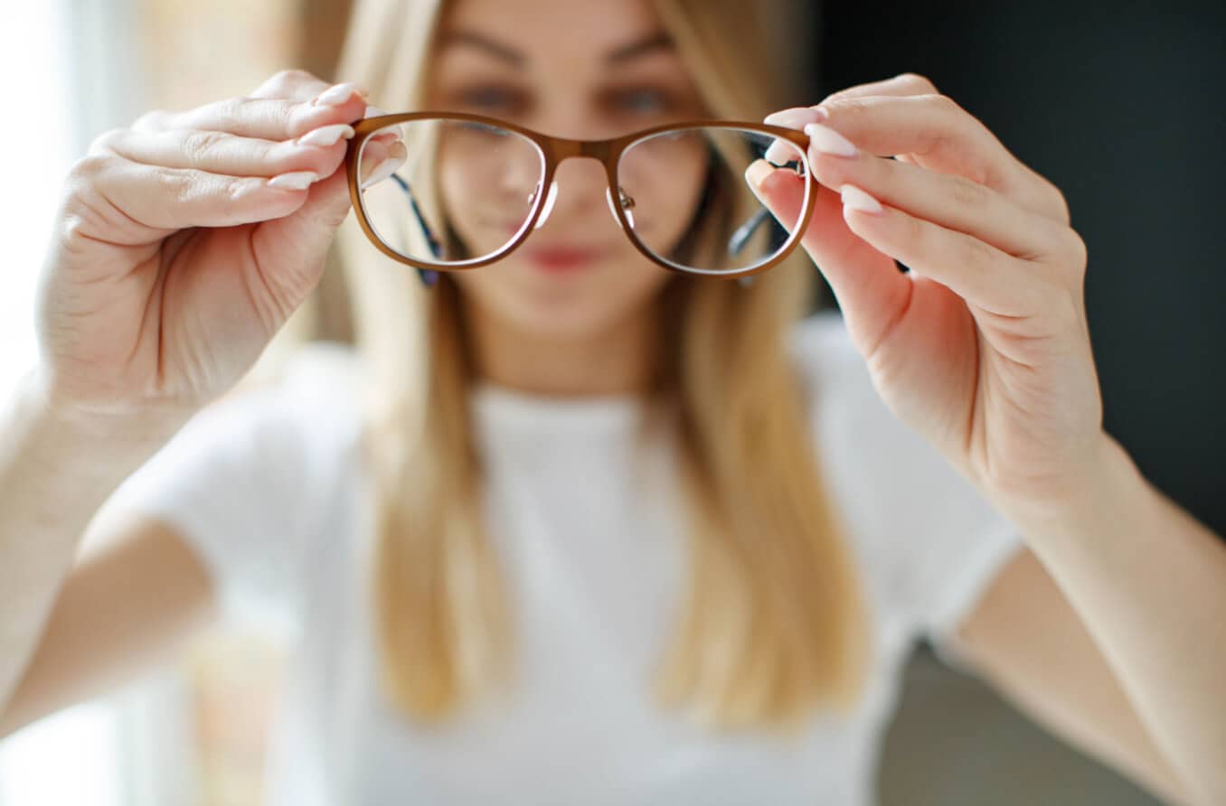 Mädchen hält Brille hoch und schaut durch die Gläser