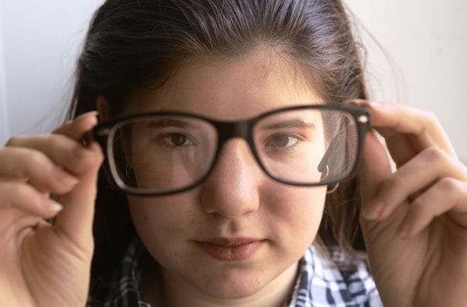 
menina de óculos segurando a armação a frente do rosto